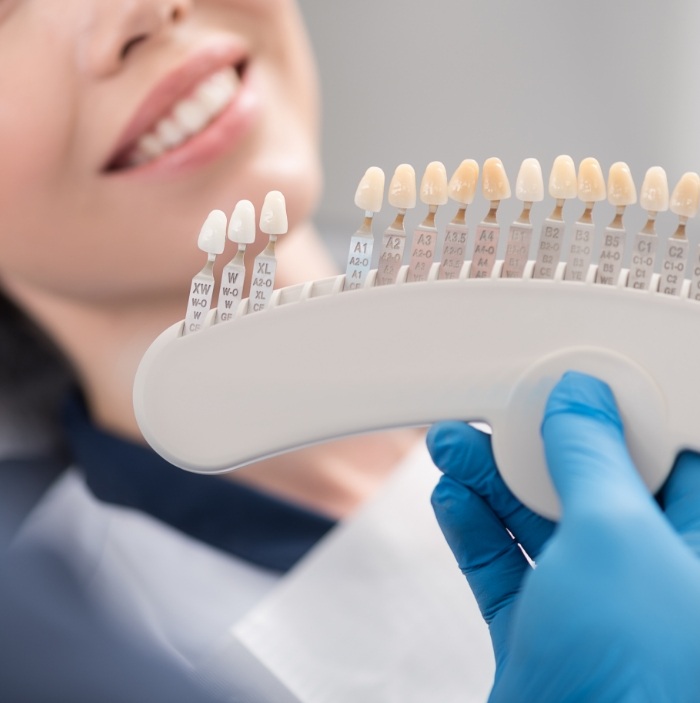 Cosmetic dentist holding shade guide in front of a patient smiling