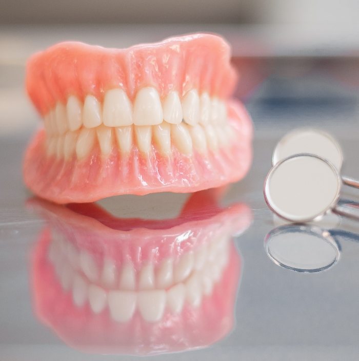 Set of full dentures on table next to two dental mirrors
