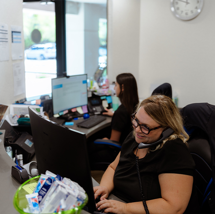 Two dental team members sitting at desk with computers